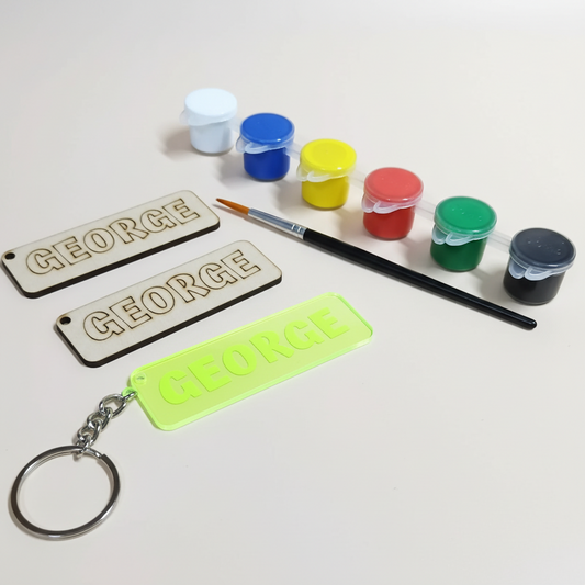 Personalized keychains and name tags on a wooden surface with paint supplies.